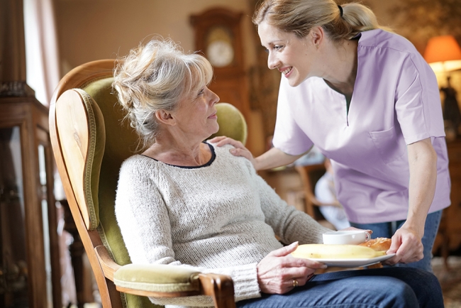 Attendant helping senior woman with meal preparation. 
